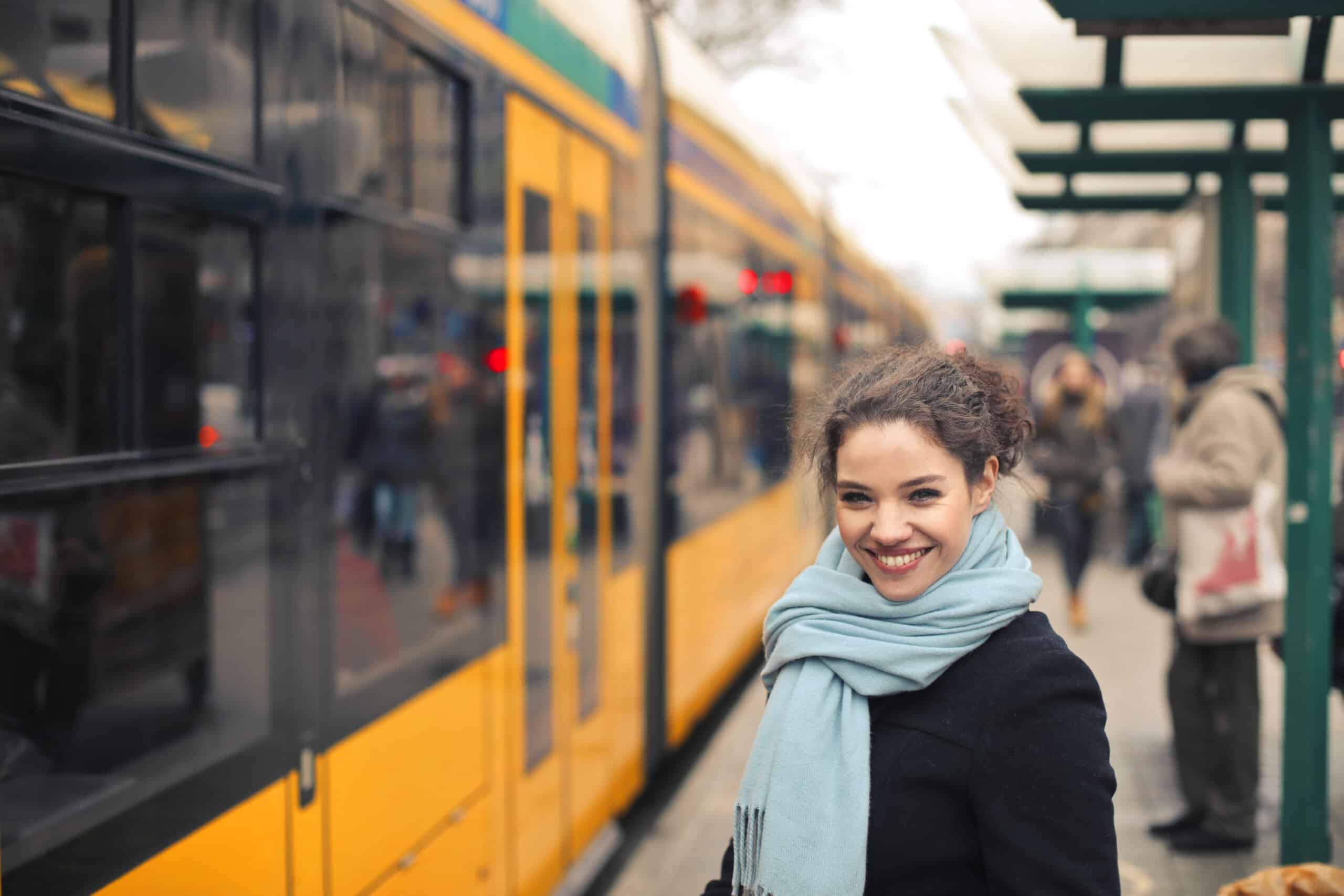 Eine Junge Frau steht am Bahnsteig HNV und lächelt in die Kamera, Am Bahnsteig wartet die Stadtbahn schon das die Fahrgäste einsteigen